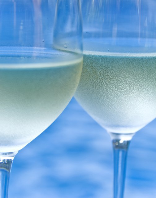 Dois copos de vinho branco em primeiro plano, sobre fundo azul