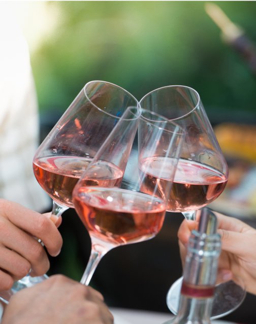 Três copos de vinho rosé a brindar ao ar livre, com fundo verde desfocado