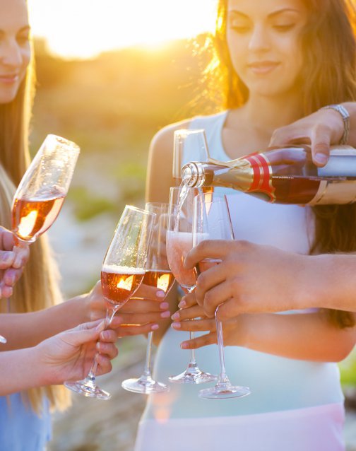 Vinho espumante a ser servido em copos segurados por um grupo de pessoas ao pôr do sol