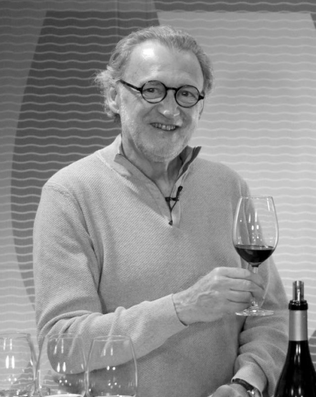 Fotografia a preto e branco de Jorge Lucki a provar vinho, segurando um copo junto a uma garrafa